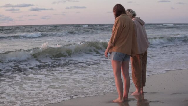 Women friends hold hands by the sea at sunset in the summer. Romantic walk of LGBT couples