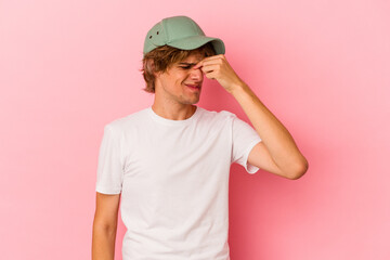 Young caucasian man with make up isolated on pink background having a head ache, touching front of the face.