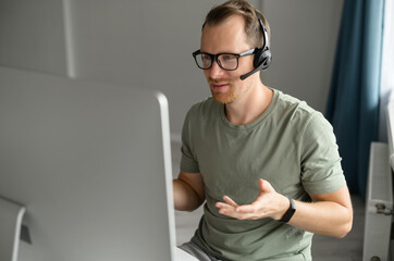 Young male employee wearing headset talking online with a colleagues or customers, freelancer man...
