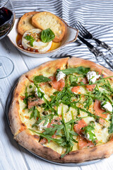 Pizza with mozzarella, salmon slices, fresh arugula. Served with baked cheese camembert and red wine. Italian cuisine