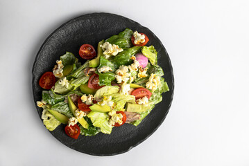 Plate of fresh and healthy summer avocado and tomatoes salad with fresh greenery and popcorn.