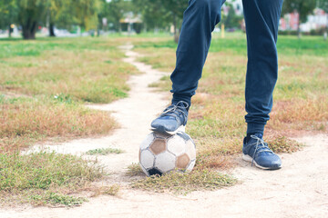 Old Soccer ball with teenager feet on the football field. Selective focus.