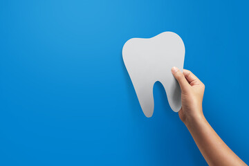 Close up hand holding tooth icon.