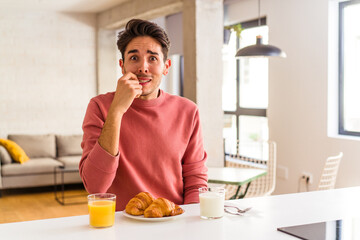 Fototapeta na wymiar Young mixed race man having breakfast in a kitchen on the morning biting fingernails, nervous and very anxious.