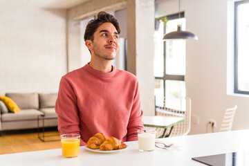 Fototapeta na wymiar Young mixed race man having breakfast in a kitchen on the morning dreaming of achieving goals and purposes
