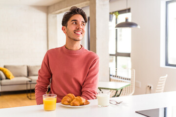 Fototapeta na wymiar Young mixed race man having breakfast in a kitchen on the morning looks aside smiling, cheerful and pleasant.