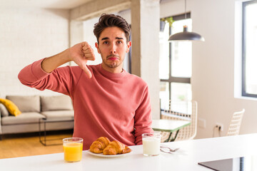 Young mixed race man having breakfast in a kitchen on the morning showing a dislike gesture, thumbs down. Disagreement concept.