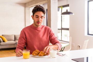 Young mixed race man eating croissant in a kitchen on the morning