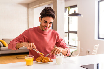 Fototapeta na wymiar Young mixed race man eating croissant in a kitchen on the morning
