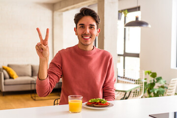 Young mixed race man having breakfast in his kitchen showing number two with fingers.