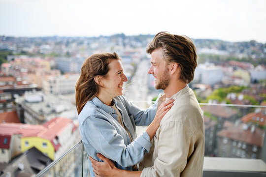 Happy young couple in love standing outdoors on balcony at home, looking at each other.