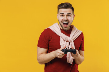Fototapeta na wymiar Excited impressed young man 20s in red t-shirt casual clothes hold in hand play pc game with joystick console isolated on plain yellow color wall background studio portrait. People lifestyle concept