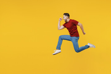 Fototapeta na wymiar Full length profile overjoyed happy young man 20s in red t-shirt casual clothes jump high clench fists run fast isolated on plain yellow color wall background studio portrait People lifestyle concept