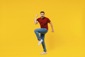 Fototapeta na wymiar Full length happy overjoyed excited caucasian young man 20s wear red t-shirt casual clothes doing winner gesture clench fist celebrating isolated on plain yellow color wall background studio portrait