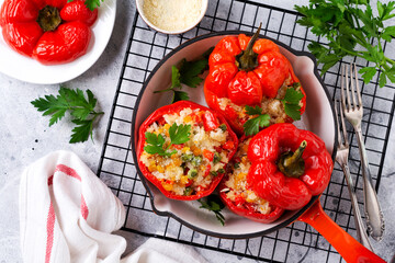 Red bell peppers stuffed with rice and vegetables on cast iron pan on gray concret background
