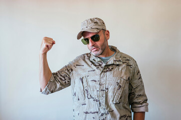 Caucasian man in camouflaged military uniform showing his arm, strength concept.