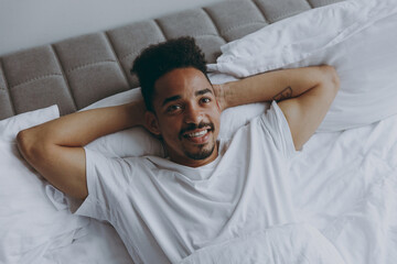 Top view from above pensive minded calm young african american man in nightwear lying in bed rest relax spend time in bedroom lounge home in own room house wake up dream be lost in reverie good day