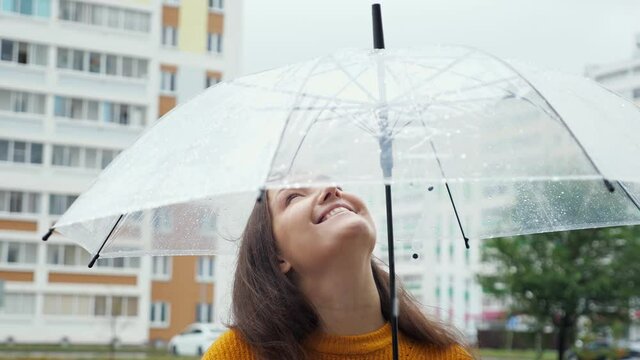 happy young woman stands under transparent umbrella in the rain.