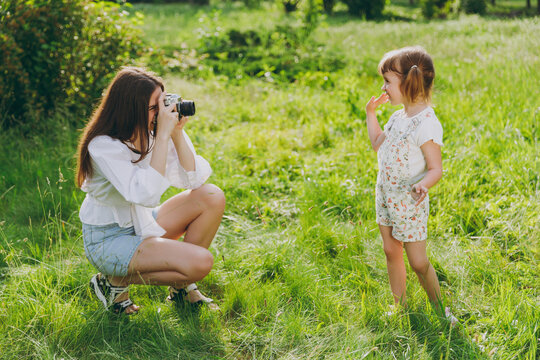 Smiling photographer young woman wear white clothes take picture shot on mobile cell phone of child baby girl 5-6 years old Mommy rest with little kid daughter outdoor together. Love family concept