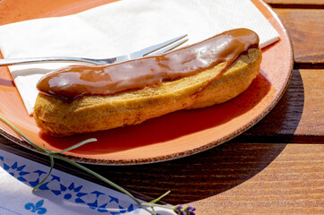 High-angle shot of a delicious eclair with a caramel topping on a wooden table in the outdoor cafe
