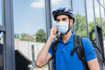 Arabian deliveryman in bike helmet and medical mask talking on smartphone on urban street © LIGHTFIELD STUDIOS