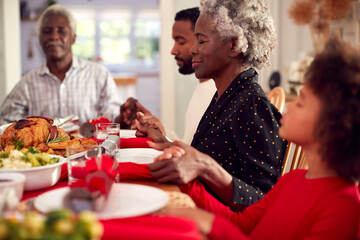 Multi Generation Family Hold Hands Around Table At Home Saying Grace Before Eating Christmas Meal