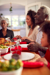 Multi Generation Family Hold Hands Around Table At Home Saying Grace Before Eating Christmas Meal