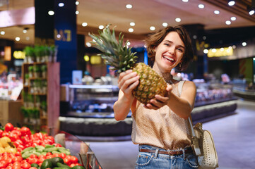 Young fun smiling happy woman 20s wear casual clothes shopping at supermaket greengrocery store buy giving hold exotic pineapple fruit inside hypermarket. People lifestyle purchasing food concept - Powered by Adobe