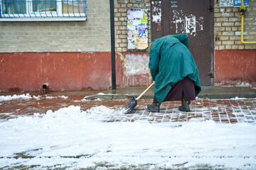 An old grandma yard man clears the snow on entrance
