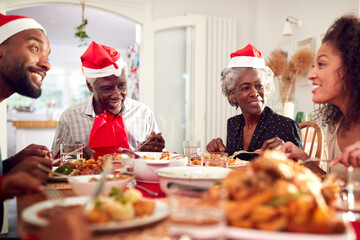 Multi Generation Family In Paper Hats Enjoying Eating Christmas Meal At Home Together