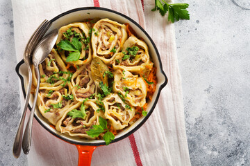 Meat dough rolls with meat or lazy dumplings in a cast-iron pan on an old rustic wooden background. Top view