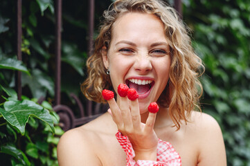 Close up young wistful happy excited woman 20s in pink dress put girl put raspberries on fingers...