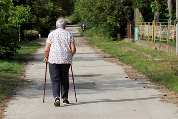 Old woman walking with a cane on a street. Limping person, diseases of the spine, life of elderly people