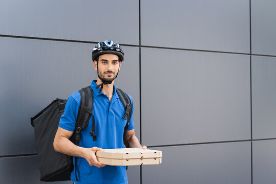 Arabian courier in helmet holding pizza boxes near building outdoors