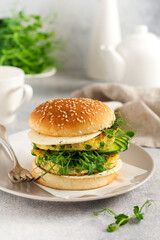 Healthy Vegetarian burger with egg and pea shoots and seeds microgreen, fresh salad, cucumber slice on a cutting wooden board on light background. Selective focus