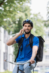 Young muslim deliveryman with backpack talking on smartphone