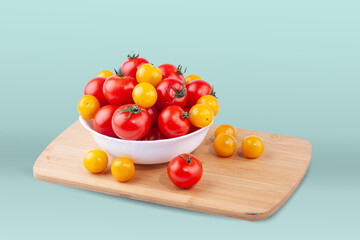 Yellow and red tomatoes in a plate on a cutting board. On a blue background.