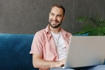 Young smiling happy minded fun man in casual clothes hold use work on laptop pc computer look aside...