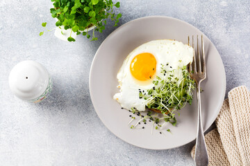 Fried eggs with arugula microgreen in gray ceramic plate on gray concrete old background. Traditional English breakfast. Top view