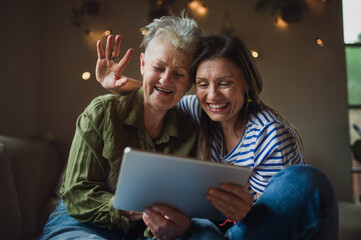 Fototapeta premium Portrait of happy senior mother with adult daughter indoors at home, using tablet.