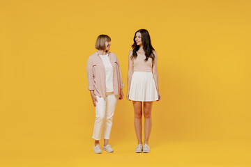 Full body two young smiling fun daughter mother together couple women in casual beige clothes looking to each other isolated on plain yellow color background studio portrait Family lifestyle concept.