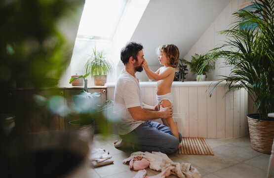 Mature father with small daughter indoors at home, getting ready for a bath.