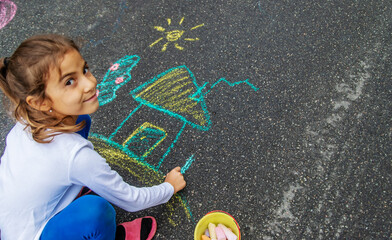 The child draws with chalk on the asphalt. Selective focus.