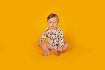 a beautiful little blue-eyed boy with light red hair in a bodysuit sits on a yellow background