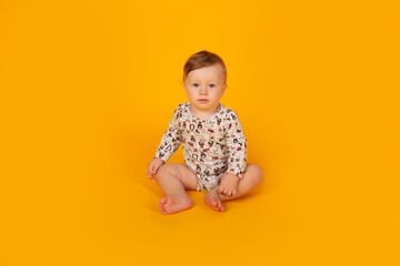 a beautiful little blue-eyed boy with light red hair in a bodysuit sits on a yellow background