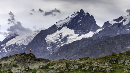 Fototapeta na wymiar Paysage de montagne présentant un jeune garçon sur un rocher devant un sommet enneigé