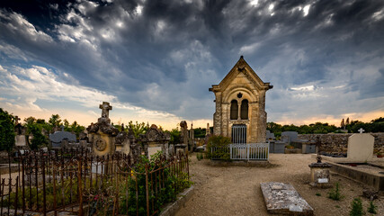 Fototapeta na wymiar Photographie d'un cimetière (Grignan) présentant une jolie chapelle prise au coucher du soleil sous un ciel d'orage gris menaçant