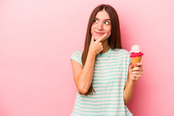 Obraz na płótnie Canvas Young caucasian woman holding an ice cream isolated on pink background looking sideways with doubtful and skeptical expression.
