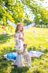 Cheerful mother and daughter having fun on child birthday on blanket with paper decorations in the park