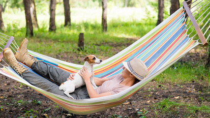 Caucasian woman lies in a hammock with Jack Russell Terrier dog in a pine forest